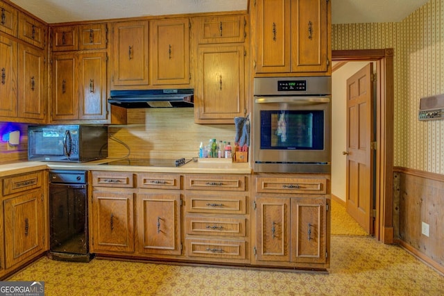 kitchen with black appliances, under cabinet range hood, light countertops, and wallpapered walls