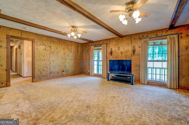 unfurnished living room with wooden walls, ceiling fan, beamed ceiling, a textured ceiling, and carpet flooring