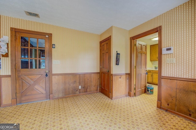 empty room featuring wallpapered walls, visible vents, and wainscoting