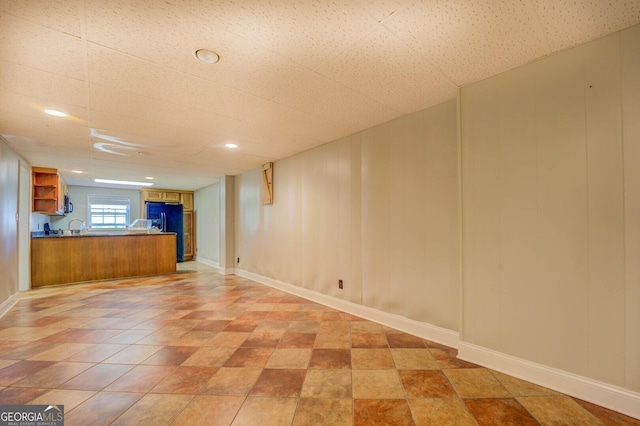 interior space with a sink, baseboards, a drop ceiling, and black fridge