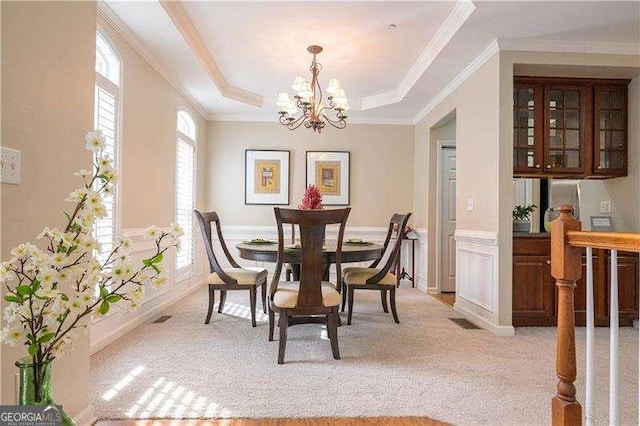 dining room featuring ornamental molding, light carpet, an inviting chandelier, and a tray ceiling