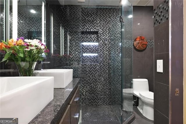 bathroom featuring tile patterned floors, toilet, an enclosed shower, tile walls, and vanity