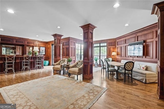 living room with light hardwood / wood-style flooring, ornamental molding, decorative columns, and indoor bar