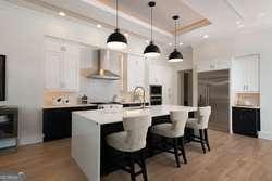 kitchen featuring wall chimney range hood, a kitchen breakfast bar, white cabinets, a kitchen island, and decorative light fixtures