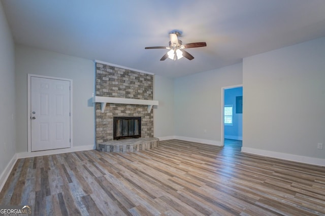 unfurnished living room featuring ceiling fan, a brick fireplace, and light wood-type flooring