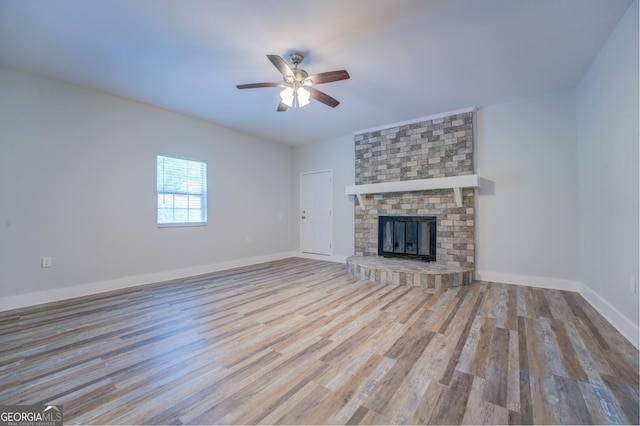 unfurnished living room with ceiling fan, a brick fireplace, and light wood-type flooring