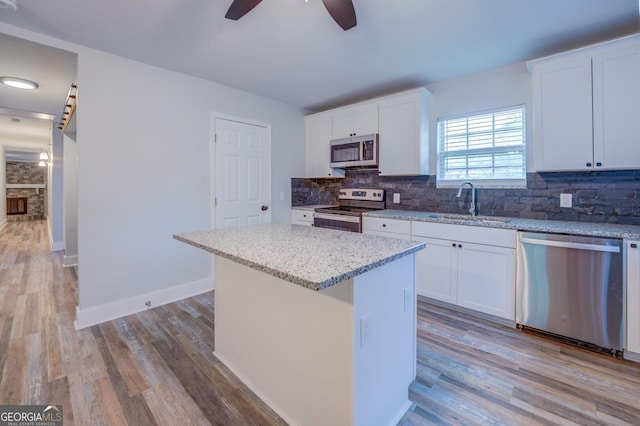 kitchen featuring a kitchen island, white cabinets, backsplash, stainless steel appliances, and light stone countertops