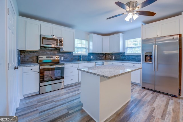 kitchen featuring white cabinetry, appliances with stainless steel finishes, a center island, and light stone countertops