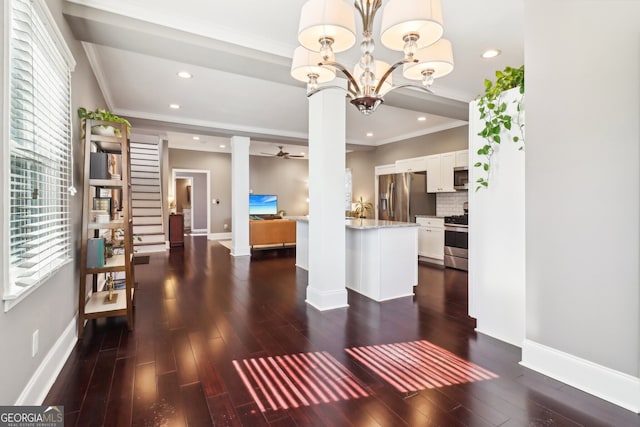 unfurnished living room featuring ornate columns, crown molding, dark hardwood / wood-style floors, and ceiling fan with notable chandelier