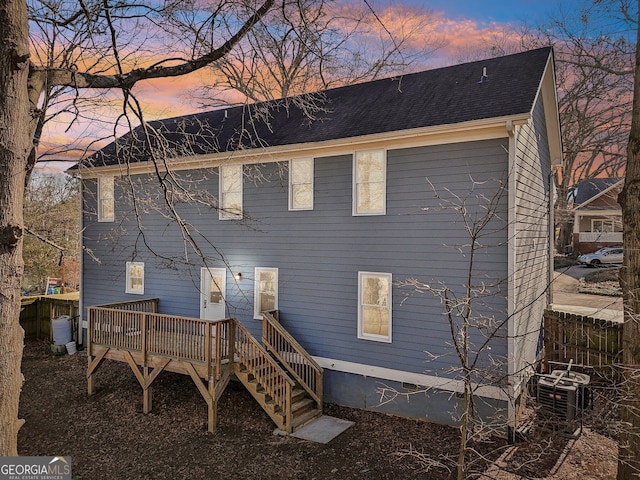 back house at dusk with a wooden deck and cooling unit