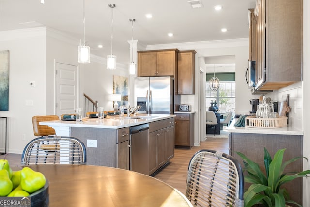 kitchen featuring sink, appliances with stainless steel finishes, a kitchen island with sink, hanging light fixtures, and light wood-type flooring