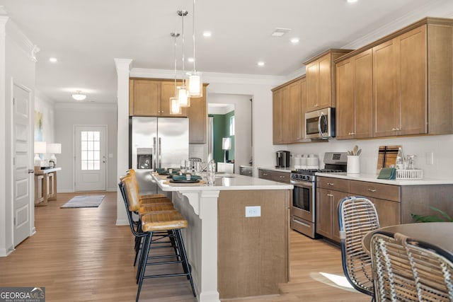 kitchen featuring appliances with stainless steel finishes, an island with sink, a breakfast bar area, hanging light fixtures, and ornamental molding