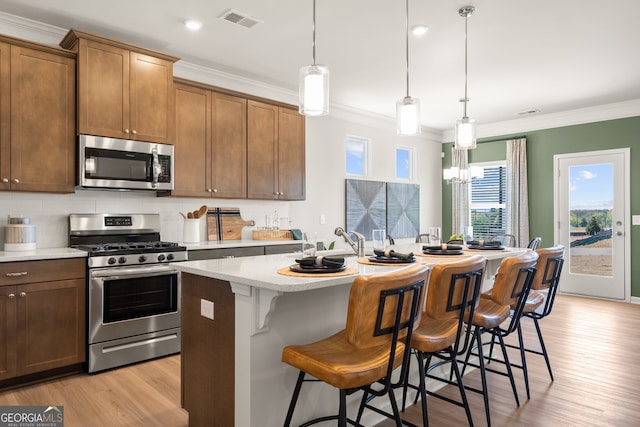 kitchen with crown molding, a kitchen island with sink, stainless steel appliances, a kitchen bar, and decorative light fixtures