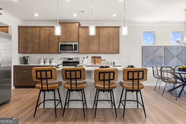 kitchen featuring pendant lighting, ornamental molding, stainless steel appliances, and a center island with sink