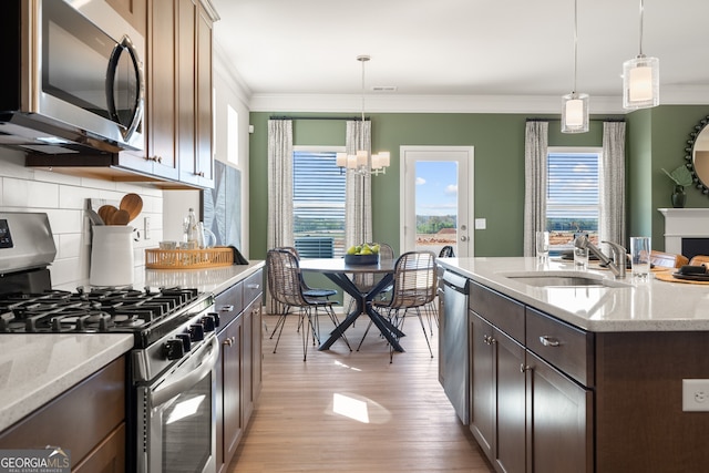 kitchen with sink, stainless steel appliances, hanging light fixtures, and an island with sink