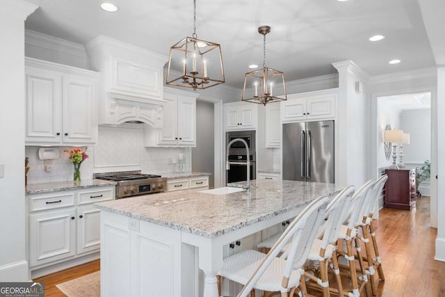 kitchen with stainless steel appliances, an island with sink, hanging light fixtures, and white cabinets