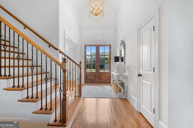 foyer with a notable chandelier, a towering ceiling, light hardwood / wood-style flooring, and french doors