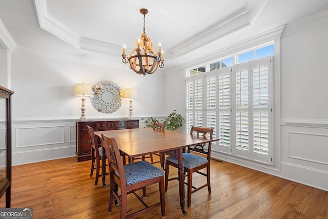 dining space with a raised ceiling, ornamental molding, a chandelier, and light wood-type flooring