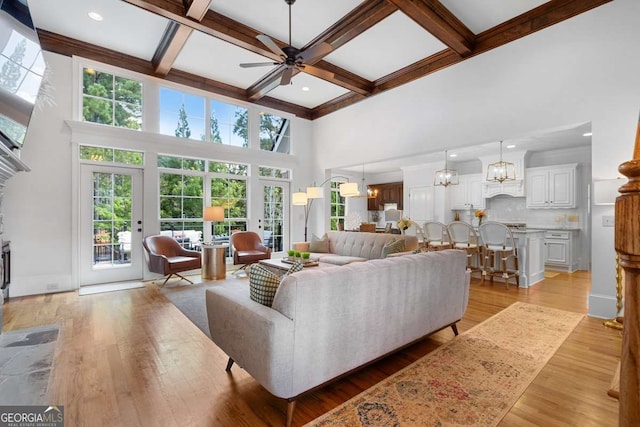 living room with a towering ceiling, ceiling fan with notable chandelier, coffered ceiling, beam ceiling, and light hardwood / wood-style flooring