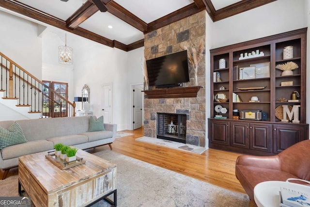 living room featuring coffered ceiling, a stone fireplace, light hardwood / wood-style flooring, a notable chandelier, and beamed ceiling