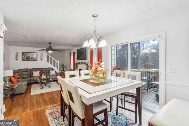 dining space with ceiling fan with notable chandelier, hardwood / wood-style floors, and a textured ceiling