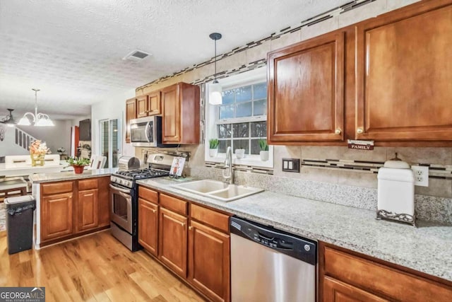 kitchen featuring appliances with stainless steel finishes, sink, light wood-type flooring, hanging light fixtures, and a textured ceiling