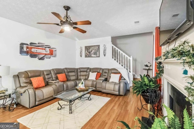 living room with hardwood / wood-style flooring, ceiling fan, and a textured ceiling