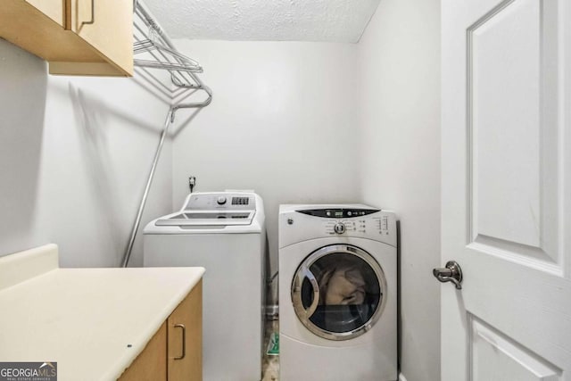 laundry area featuring cabinets, washing machine and clothes dryer, and a textured ceiling