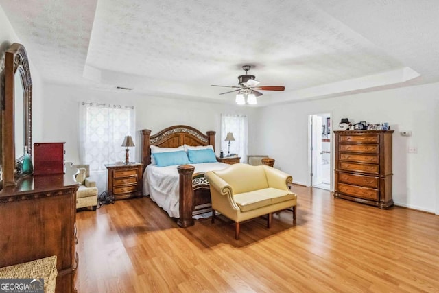 bedroom with hardwood / wood-style flooring, ceiling fan, a textured ceiling, and a tray ceiling