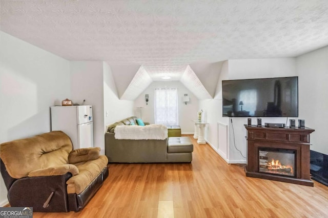 living room featuring vaulted ceiling, light hardwood / wood-style floors, and a textured ceiling