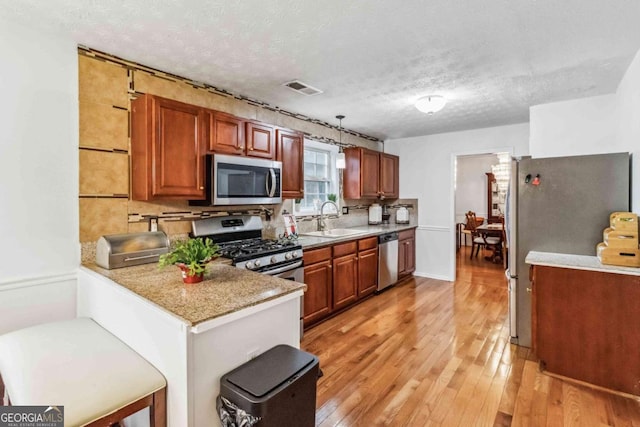 kitchen with kitchen peninsula, sink, light stone counters, light hardwood / wood-style floors, and stainless steel appliances