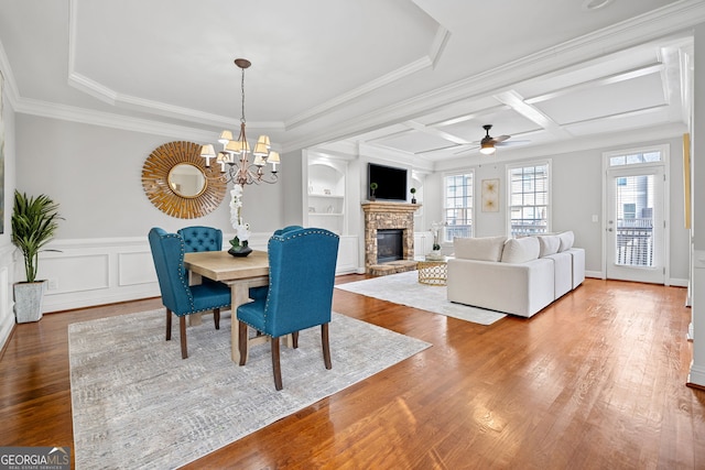 dining room with built in features, crown molding, a stone fireplace, wood finished floors, and coffered ceiling