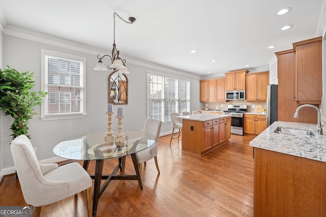 kitchen with light wood-style floors, crown molding, stainless steel appliances, and a sink