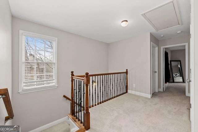 hall featuring attic access, baseboards, light colored carpet, and an upstairs landing