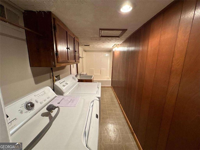 washroom featuring wooden walls, sink, cabinets, independent washer and dryer, and a textured ceiling