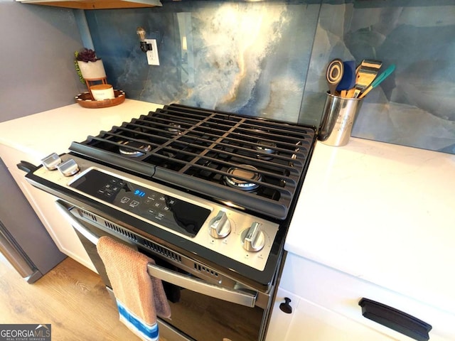 interior details with light hardwood / wood-style floors, decorative backsplash, and stainless steel gas range oven