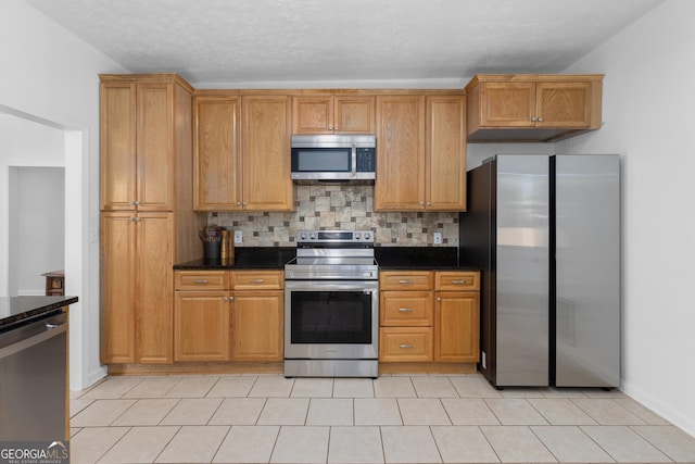 kitchen with a textured ceiling, light tile patterned floors, dark stone countertops, appliances with stainless steel finishes, and decorative backsplash