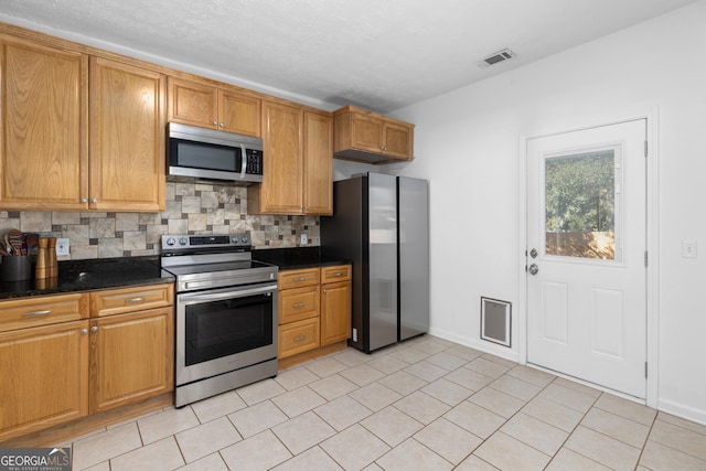 kitchen with tasteful backsplash, light tile patterned floors, stainless steel appliances, and dark stone counters