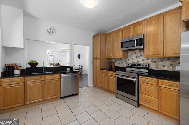 kitchen featuring sink, dark stone countertops, backsplash, stainless steel appliances, and a textured ceiling