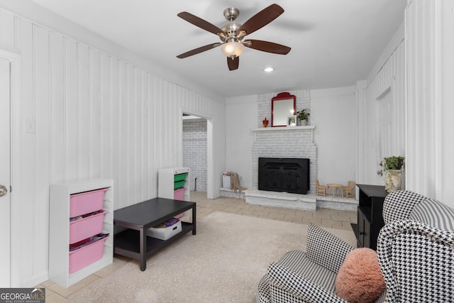 living room with ceiling fan, a brick fireplace, and light tile patterned floors