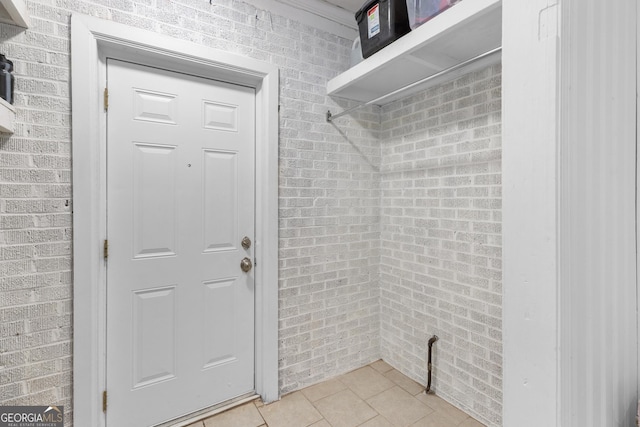 laundry area featuring brick wall and light tile patterned floors