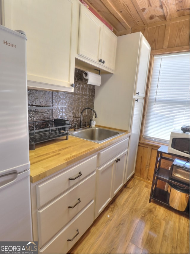 kitchen featuring white appliances, wood counters, light wood-style floors, white cabinetry, and a sink