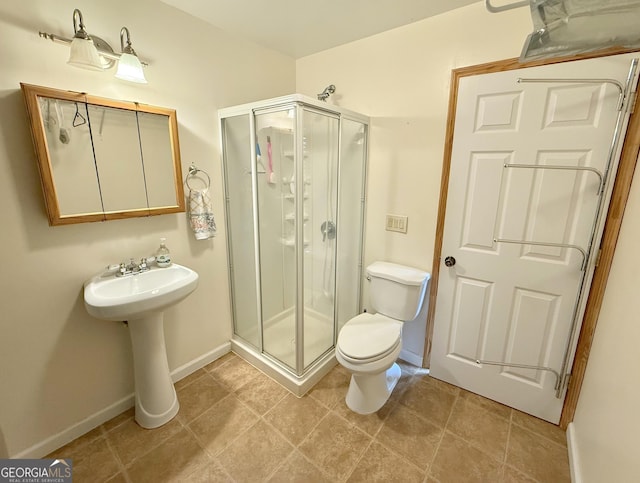 bathroom featuring a stall shower, a sink, toilet, and baseboards