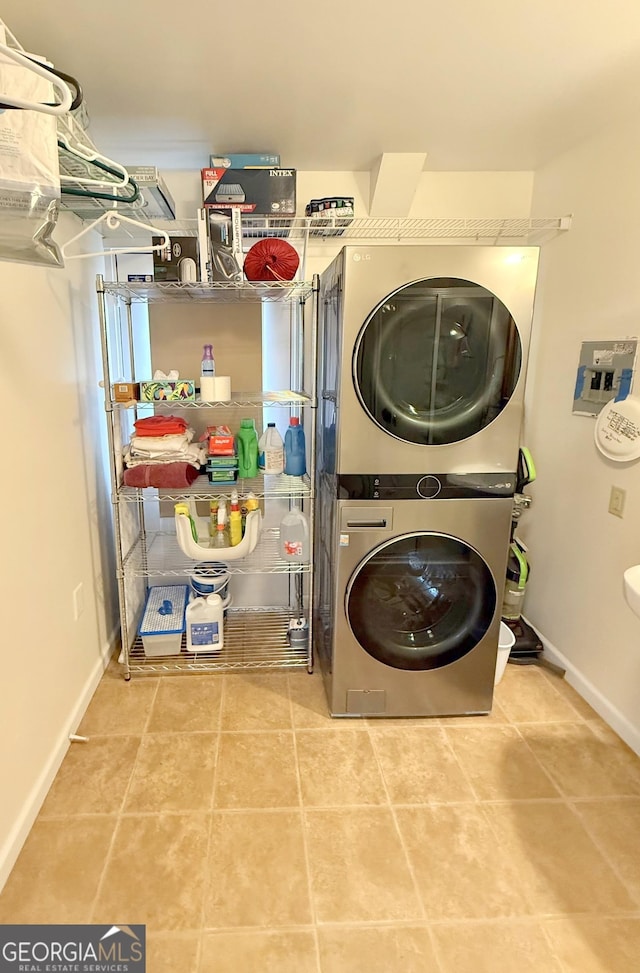 laundry room with tile patterned flooring, laundry area, baseboards, and stacked washing maching and dryer