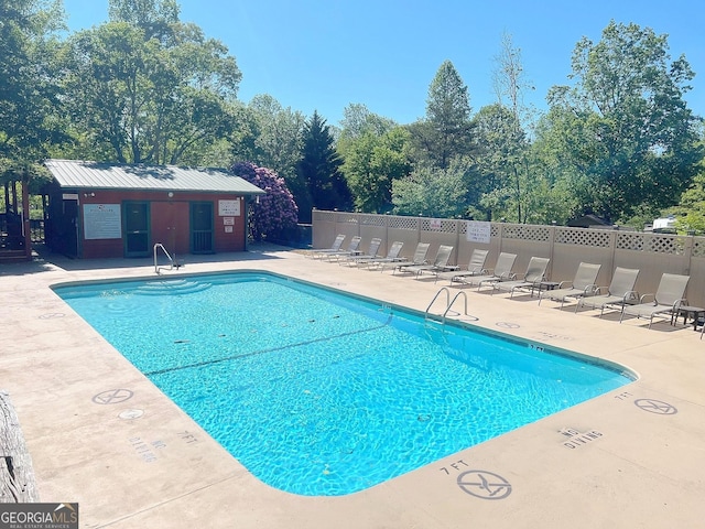 community pool with a patio area, fence, and an outdoor structure