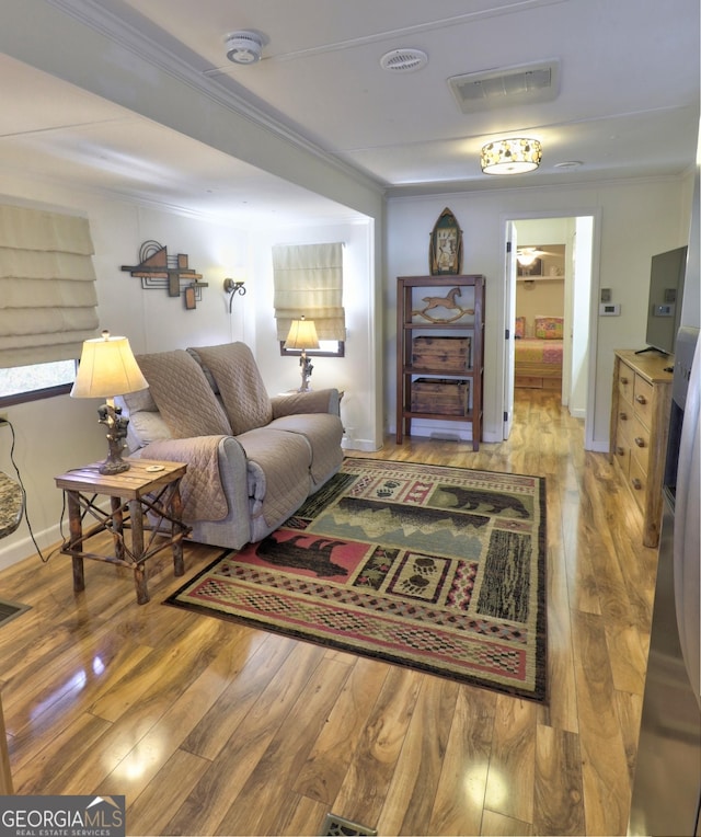 living area with visible vents, baseboards, hardwood / wood-style flooring, and crown molding