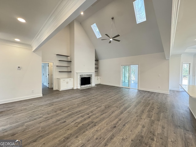 unfurnished living room with high vaulted ceiling, a skylight, a high end fireplace, crown molding, and dark wood-type flooring