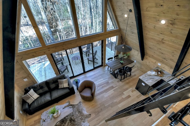 living area featuring wooden walls, beamed ceiling, a high ceiling, and wood finished floors