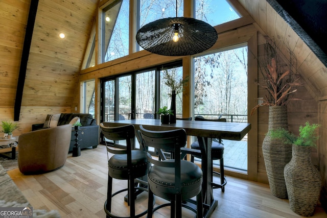 dining room featuring high vaulted ceiling, wood walls, wood ceiling, and light wood-style floors