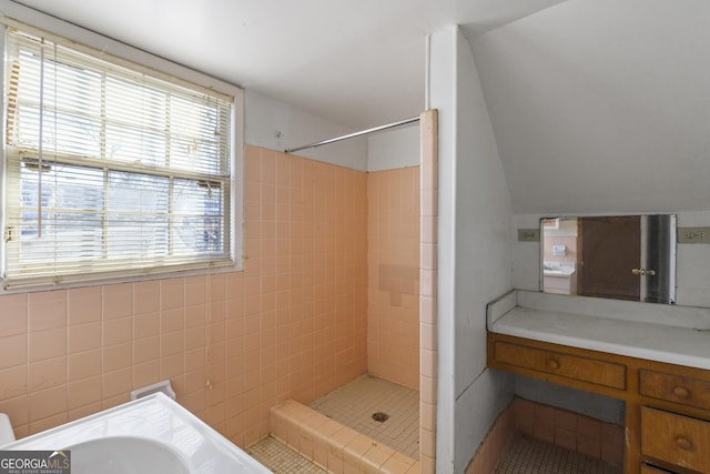 bathroom with tiled shower, vanity, and lofted ceiling